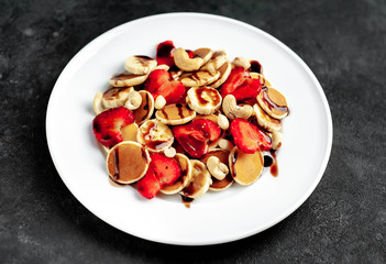 Mini pancakes with strawberries, bananas, nuts in a plate on a stone background. delicious breakfast concept