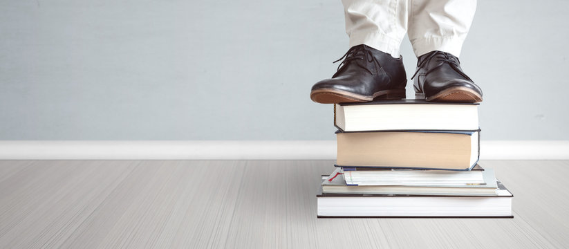 Education concept - feet standing on a stack of  books