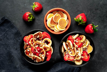 Breakfast on two. Mini pancakes with strawberries, bananas, nuts in a plate on a stone background