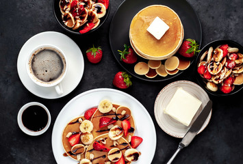 The concept of a delicious breakfast. Coffee and mini pancakes with strawberries, bananas, nuts in a plate and American pancakes in a plate on a stone background 
