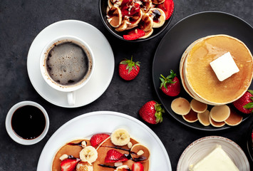 The concept of a delicious breakfast. Coffee and mini pancakes with strawberries, bananas, nuts in a plate and American pancakes in a plate on a stone background 