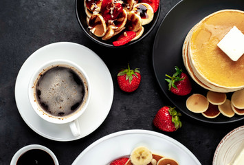 The concept of a delicious breakfast. Coffee and mini pancakes with strawberries, bananas, nuts in a plate and American pancakes in a plate on a stone background 