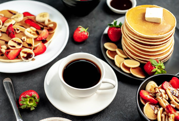The concept of a delicious breakfast. Coffee and mini pancakes with strawberries, bananas, nuts in a plate and American pancakes in a plate on a stone background 