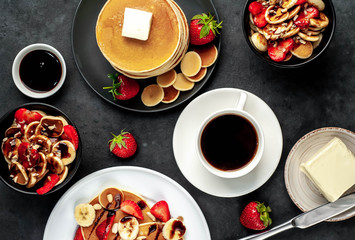 The concept of a delicious breakfast. Coffee and mini pancakes with strawberries, bananas, nuts in a plate and American pancakes in a plate on a stone background 