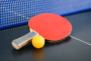 Red racquet with orange table tennis ball put on the table with blue net for ready  to play ping pong
