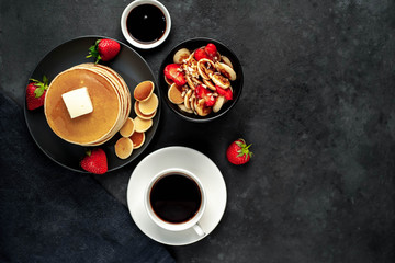 Obraz na płótnie Canvas The concept of a delicious breakfast. Coffee and mini pancakes with strawberries, bananas, nuts in a plate and American pancakes in a plate on a stone background with copy space for your text