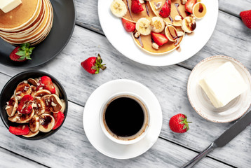 The concept of a delicious breakfast. Coffee and mini pancakes with strawberries, bananas, nuts in a plate and American pancakes in a plate on a wooden background