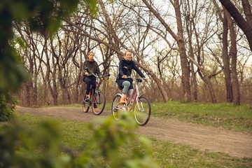 Fototapeta premium Best friends having fun near countryside park, riding bikes, spending time healthy. Calm nature, spring day, positive emotions. Sportive, active leisure activity. Traveling or walking together.