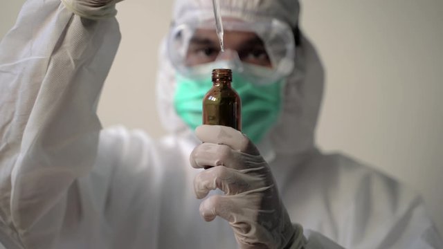 Corononavirus concept. Technician carefully drips the solution from dropper into glass bottle. 4k solution and slow motion shot.