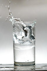 Close-up photo of the ice falls into the water glass causing water to splash out and the white background