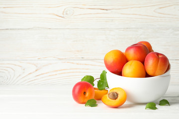 Bowl with tasty apricots on white wooden background