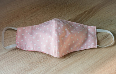 Obraz premium Handmade face masks made from cloth placed pink on wooden table, washable and reusable, can be used during shortage of surgical mask due to coronavirus pandemic. virus covid-19.