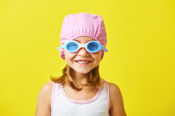 Smiling little girl in swimming cap and glasses on colored background.
