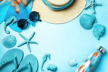 Naklejka premium Summer fashion on blue and coral background. Blue flip flops, seashells, sunglasses, bottle and straw hat. Flat lay, top view with copy space.