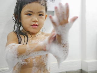 Little baby girl, 3 years old, enjoys playing soap foam / bubbles in a bathroom at home - children and a bubble bath