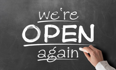 person writing text WE ARE OPEN AGAIN on chalkboard, reopening after covid-19 shutdown concept