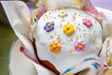 Festive Easter cake. On the home desk. Homemade baking. Decorated with white glaze. Decorated holiday table. Sweet little flowers decoration. Sunny spring day before the holiday.