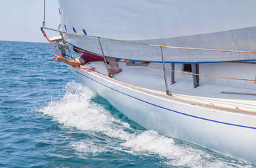 A white motor yacht with raised sails takes part in the regatta. A strong wind tipped the ship. Waves, a small wave amplify emotions at competitions. A man, a sailor, a yachtsman is lying on the bow o