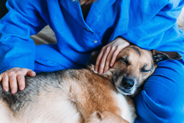 A girl in blue linen pajamas stroking a dog. The dog is relaxed and sleeping