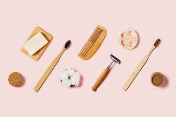Bathroom accessories on pink background. Natural bamboo toothbrushes, sponges, cotton flowers, shaving brushes. Flat lay, top view.