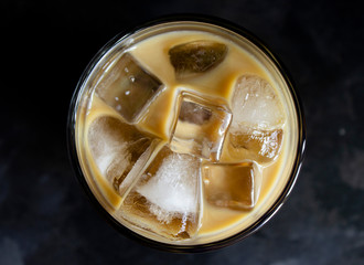 Top view on iced coffee with milk in a tumbler glass cup on a dark background
