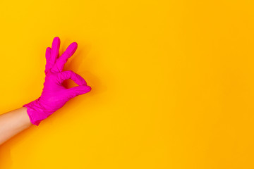 Hand in pink protective rubber glove showing nice sign isolated on yellow studio background with copyspace. Gesturing, holding, presenting things. Negative space for your advertising. Showing