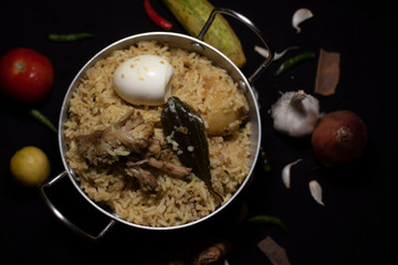Indian spicy dish Biryani with egg, potato and Chicken in a pot along with ingredients in dark copy space background. Food and object photography.