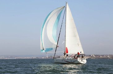 White motor yacht with raised sails takes part in the training regatta. A strong wind tipped the ship. Increase small wave of emotion in the competition. On the horizon you can see the city and the bl