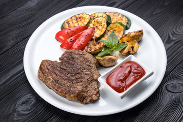 grilled steak, zucchini, on a white plate and black background