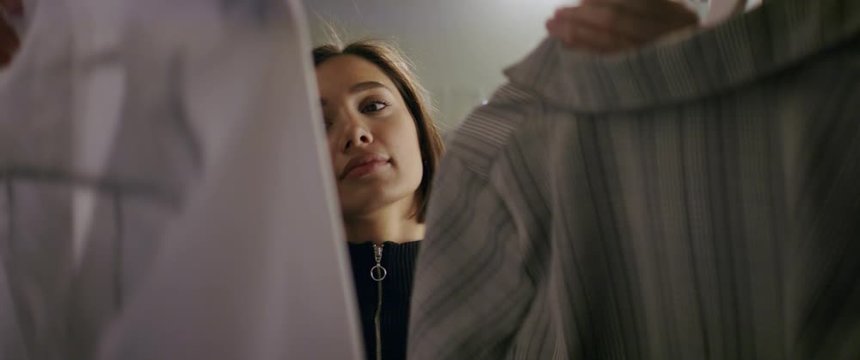 Beautiful young woman choosing clothes for work in wardrobe at home. Preparing for a date or night out. Shot with anamorphic lens