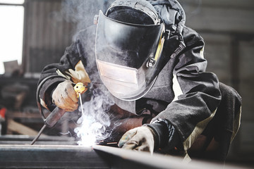 Welder working with welding on metal frames in an industrial plant.