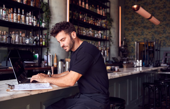 Male Owner Of Restaurant Bar Sitting At Counter Working On Laptop