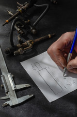 Auto mechanic draws up a drawing on a sheet of paper in a workshop.