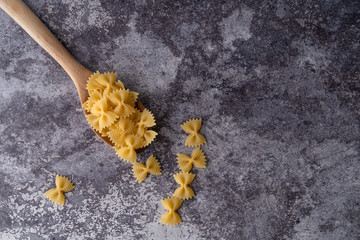 Top view of a wooden spoon full of pasta, farfalle type, on a dark marble background.