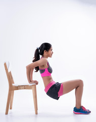 Young beautiful lady wearing exercise suit put hand touch on wooden chair and  kneel, for stretching body.