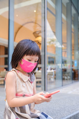 Asian child wearing mask and using cell phone in city