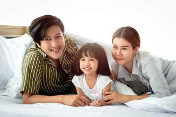 Happy family having fun in the bedroom. Father, mother and daughter lying on bed and spending time together, parents and kid having good memory and playing together at home