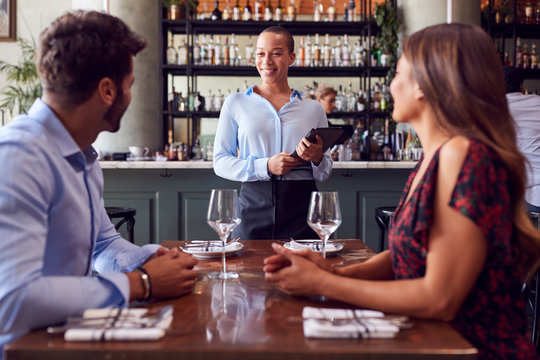 Female Waitress With Digital Tablet Taking Order From Romantic Couple Sitting At Restaurant Table