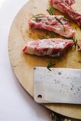 Raw Lamb Chops cut on a wooden rounded cutboard over a white background,  big butcher knife on the side