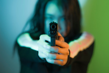edgy cinematic portrait of young attractive and dangerous special agent woman or Asian mobster girl holding handgun pointing the gun fierce in Hollywood movie style