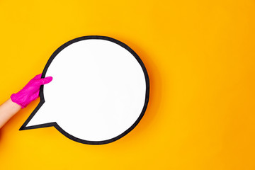 Hand in pink protective rubber glove holding comment isolated on yellow studio background with copyspace. Gesturing, holding, presenting things. Negative space for your advertising. Showing, pointing.