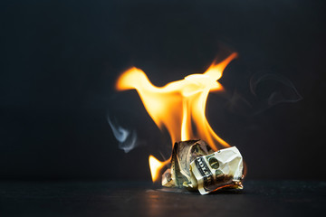 Crumpled dollar bills burning fire on a dark background