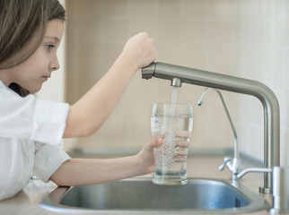 Child is holding a transparent glass. Filling cup beverage. Pouring fresh drink. Consumption of tap water contributes to the saving of water in plastic bottles and to the protection of the environment