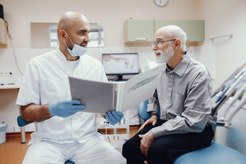 Handsome old man talking to the dendist. Two men in the dentist's office
