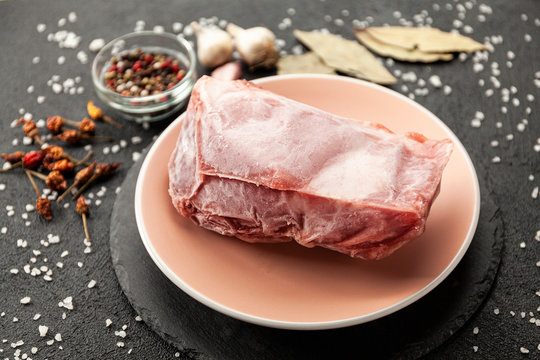 Frozen Piece Of Raw Meat On Plate On Black Table. Rime On Product, Thawing.