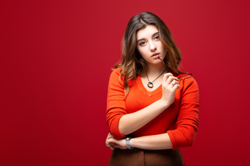 Young girl student or business woman with glasses in hands isolated on a red background. Skeptical look and mood