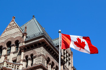 The waving Canadian flag at Old City Hall in background in Toronto, Canada. Toronto is the provincial capital of Ontario and the most populous city in Canada.  - obrazy, fototapety, plakaty
