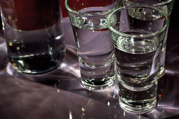 Glasses with alcohol near the bottle. Transparent drink on a purple background.