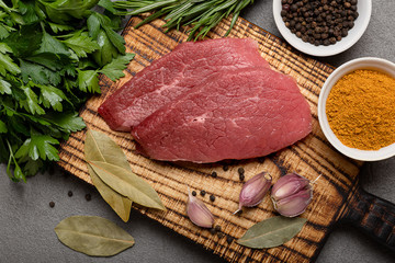 Two raw beef steaks with spices on a cutting board on black background
