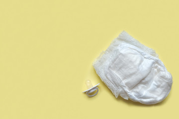  baby diaper and soother or pacifier on yellow background. Happy childhood concept. copy space for...